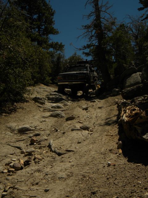 1992 Ford Bronco - A 1992 Ford Bronco navigates a challenging, rocky trail surrounded by trees and boulders.