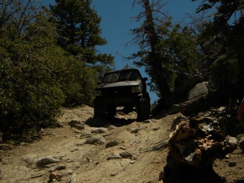 1992 Ford Bronco - 1992 Ford Bronco navigating a challenging off-road path in a wooded, mountainous area.