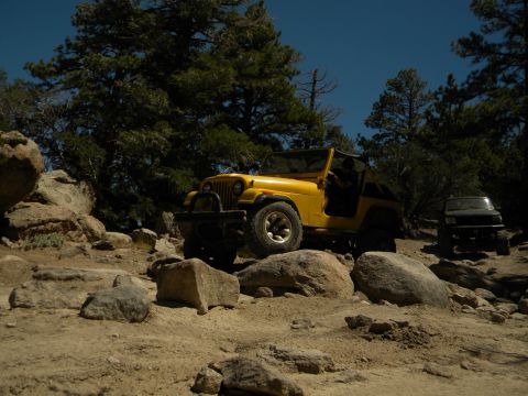 1992 Ford Bronco - A yellow Jeep Wrangler navigates a rocky trail with a black SUV behind it under a clear blue sky.