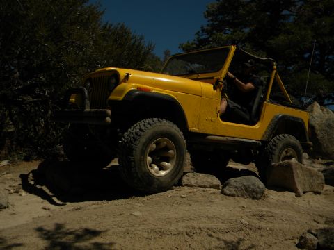 1992 Ford Bronco - A yellow Jeep CJ is shown off-road, traversing a path with large rocks.