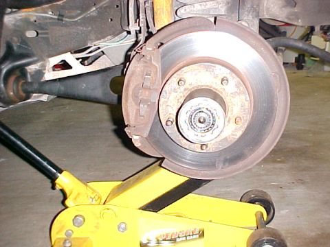 1996 Ford Bronco - Close-up view of a vehicle's front wheel hub and brake assembly, supported by a yellow hydraulic jack.