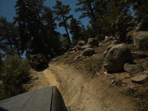 1992 Ford Bronco - Two off-road vehicles navigate a rocky dirt path through a wooded area.