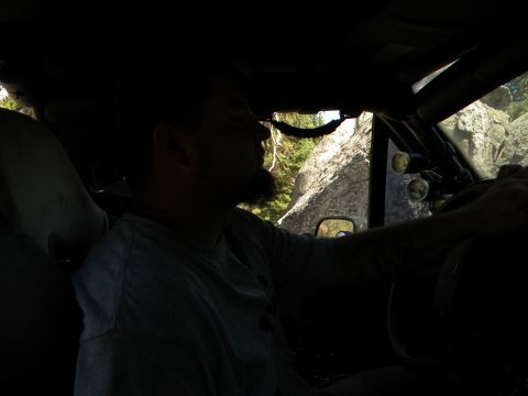 1992 Ford Bronco - Man drives an off-road vehicle through rocky terrain, with auxiliary lights mounted on the roll cage.