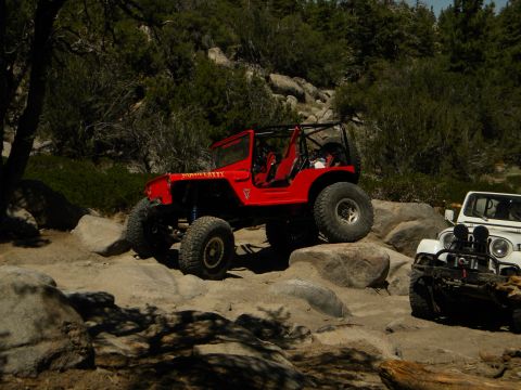 1992 Ford Bronco - A red off-road jeep navigates a rocky trail, with another white jeep visible in the background.