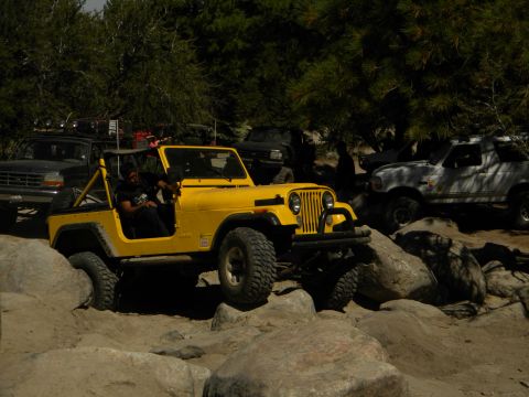 1992 Ford Bronco - A yellow Jeep CJ-7 is shown off-roading over large rocks, with other vehicles present.