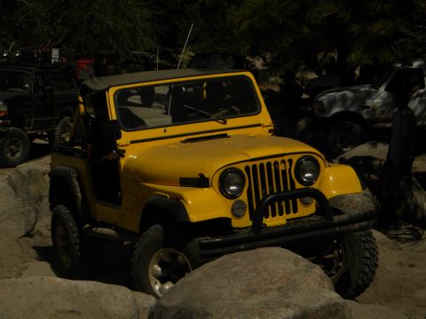 1992 Ford Bronco - A yellow Jeep CJ navigates a rocky terrain, with other vehicles visible in the background.