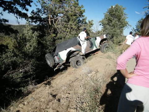 1982 Ford Bronco - A group watches as a modified off-road vehicle navigates a challenging incline on a sunny day.