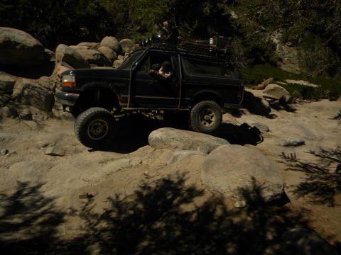 1992 Ford Bronco - A black 1992 Ford Bronco navigates a rocky trail with a lifted suspension and roof rack.