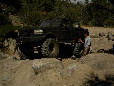 1992 Ford Bronco - A black 1992 Ford Bronco is shown off-roading on a rocky trail, demonstrating its capabilities on challenging terrain.