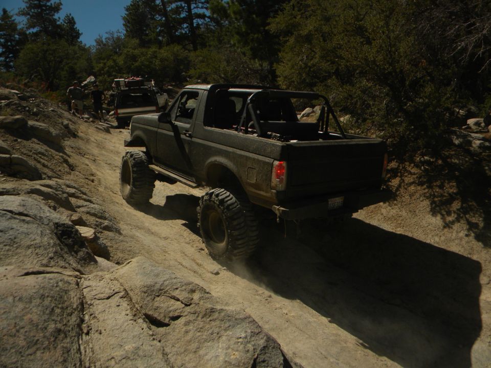 Dark 1992 Ford Bronco with roll cage and large tires on a rocky trail