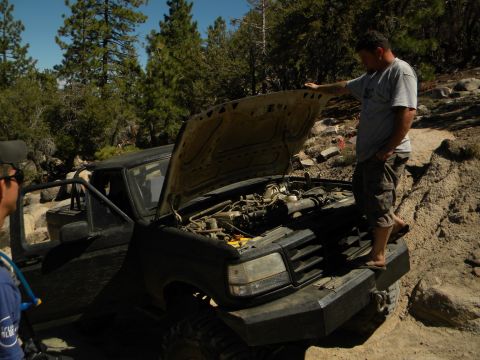 1992 Ford Bronco - A man inspects the engine of a 1992 Ford Bronco, which has a custom front bumper and is parked off-road.