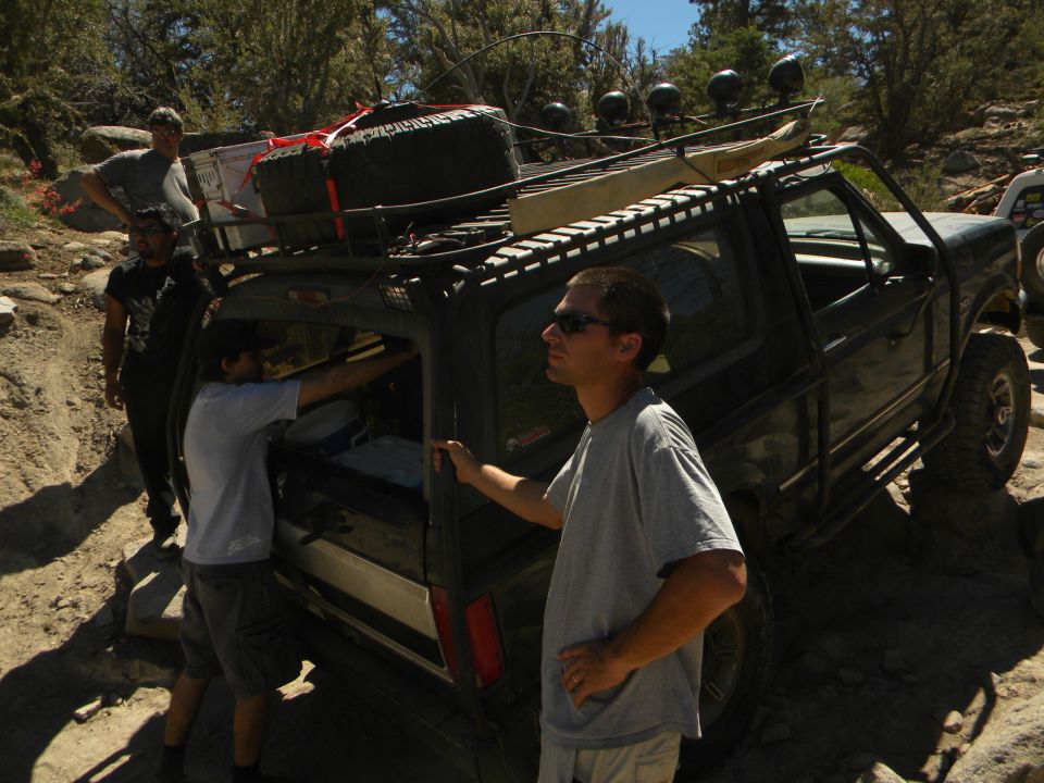 1992 Ford Bronco with roof rack and spare tire on a rocky trail, people loading gear