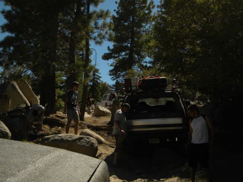 1992 Ford Bronco - Several off-road vehicles navigate a challenging rocky trail surrounded by trees and boulders.