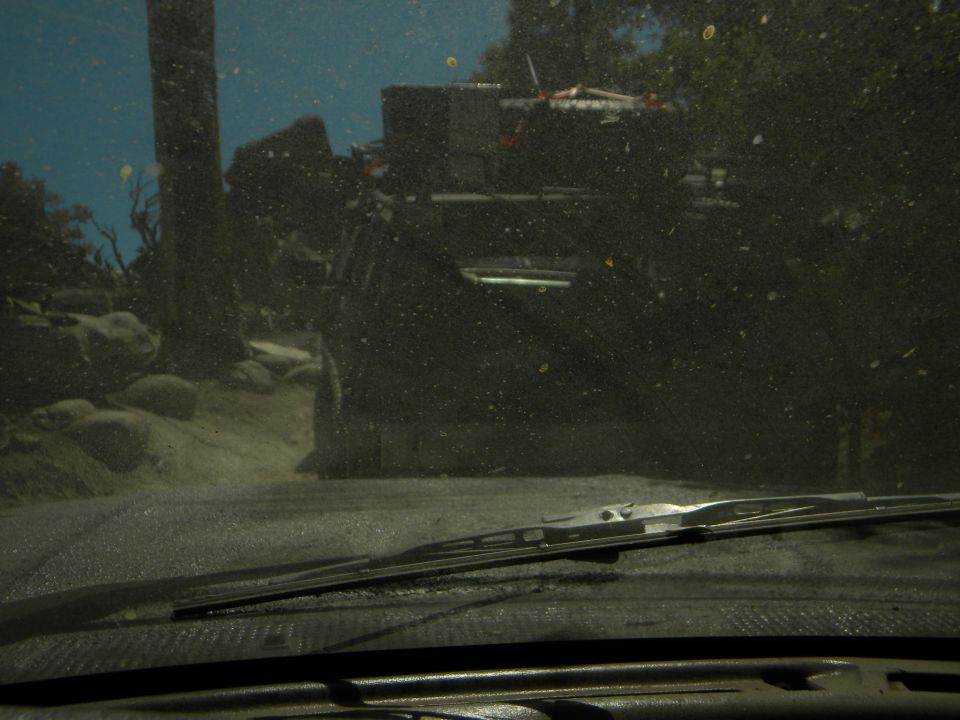 View from inside a vehicle looking out at another vehicle on a dirt road with trees and rocks