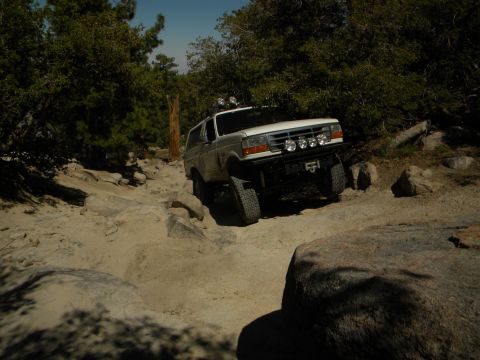 1992 Ford Bronco - A white 1992 Ford Bronco navigates a challenging rocky off-road path under a clear sky.