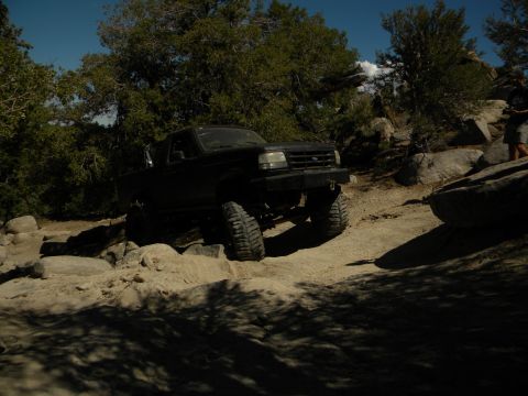 1992 Ford Bronco - A black Ford F-Series truck navigates a rocky off-road trail under a clear blue sky.