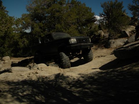 1992 Ford Bronco - A black 1992 Ford Bronco navigates a rocky trail under a clear blue sky.