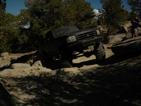 1992 Ford Bronco - A lifted black Ford F-Series truck navigates a rocky trail under a clear blue sky.