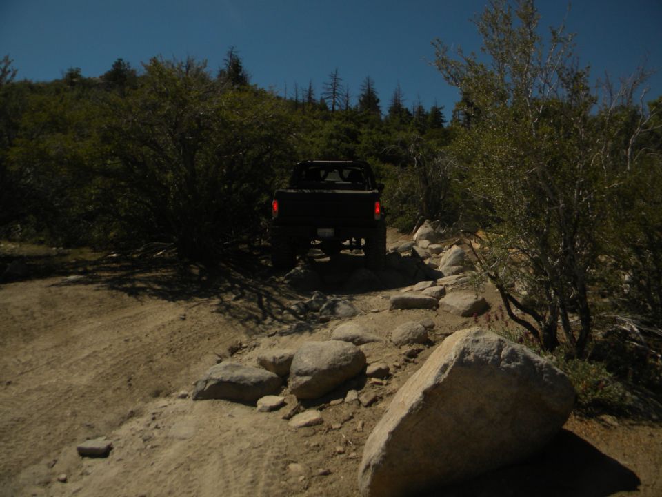 Off-road vehicle driving on a rocky, dirt trail with trees and bushes on either side