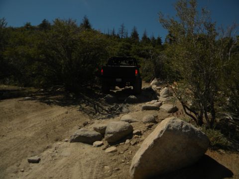 1992 Ford Bronco - A black pickup truck navigates a challenging, rocky off-road trail under a clear blue sky.