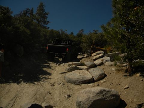 1992 Ford Bronco - A black 1992 Ford Bronco navigates a challenging, rocky off-road path surrounded by trees.