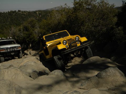 1992 Ford Bronco - A yellow Jeep Wrangler tackles a challenging rocky trail, with a white Ford Bronco visible in the background.