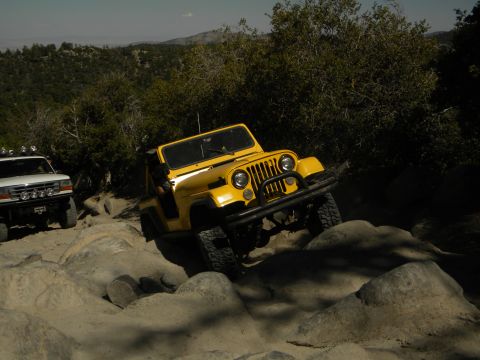 1992 Ford Bronco - Two off-road vehicles tackle a challenging rocky path in a wooded, mountainous area.