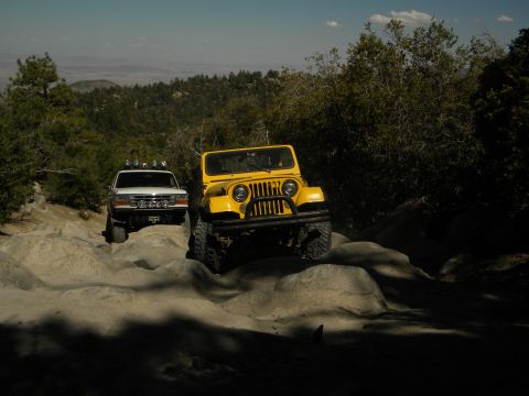 1992 Ford Bronco - Two off-road vehicles navigate a challenging rocky trail under a clear sky.