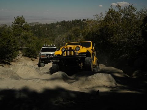 1992 Ford Bronco - Two off-road vehicles, a yellow Jeep CJ and a white Ford Bronco, tackle a challenging rocky trail in a mountainous landscape.
