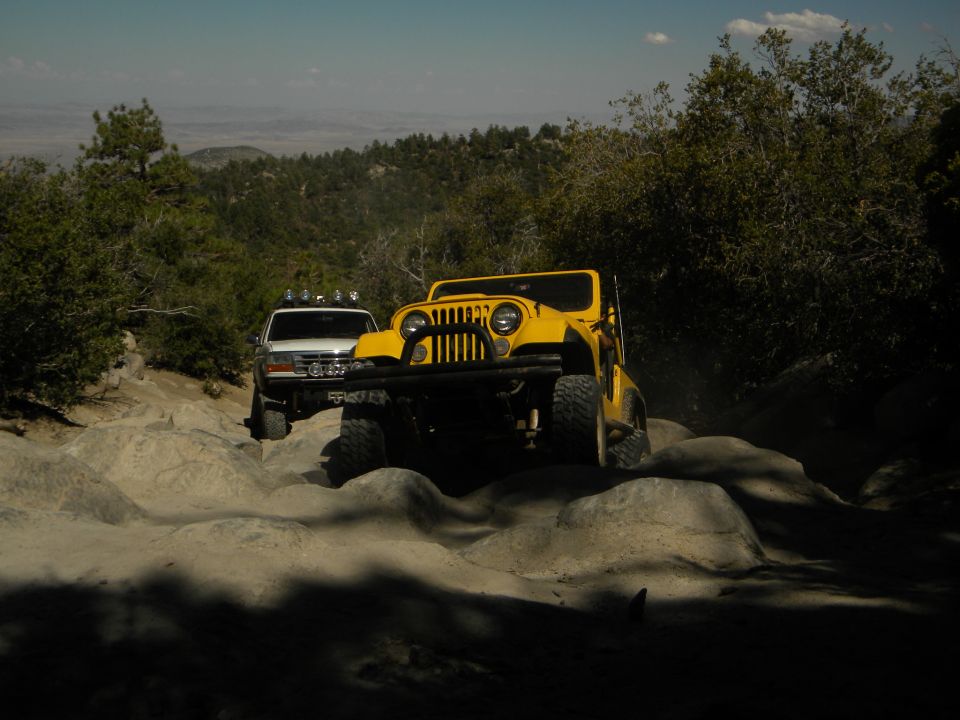 Yellow Jeep CJ and white Ford Bronco navigating rocky terrain off-road
