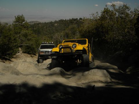 1992 Ford Bronco - Two off-road vehicles tackle a challenging rocky path in a mountainous landscape.