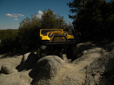 1992 Ford Bronco - A yellow Jeep Wrangler navigates a challenging rocky trail under a blue sky.