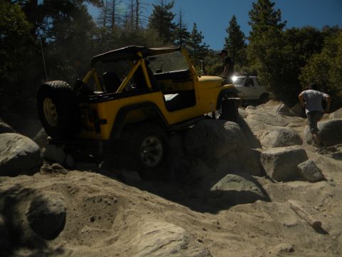 1992 Ford Bronco - A yellow Jeep Wrangler is shown off-roading on a rocky trail with another vehicle in the background.
