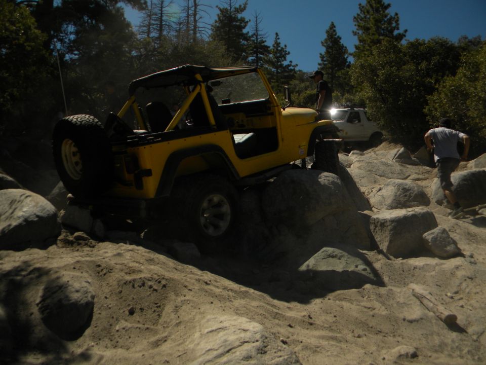 Yellow Jeep Wrangler navigating rocky terrain with a white truck behind it