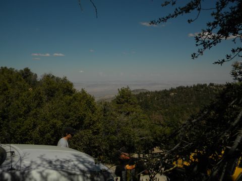 1992 Ford Bronco - A white SUV is partially visible in the foreground, parked on a dirt road with a scenic mountain view in the background.