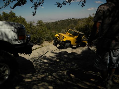 1992 Ford Bronco - A yellow jeep is stuck in the sand and being pulled out by a white truck on a sunny day.
