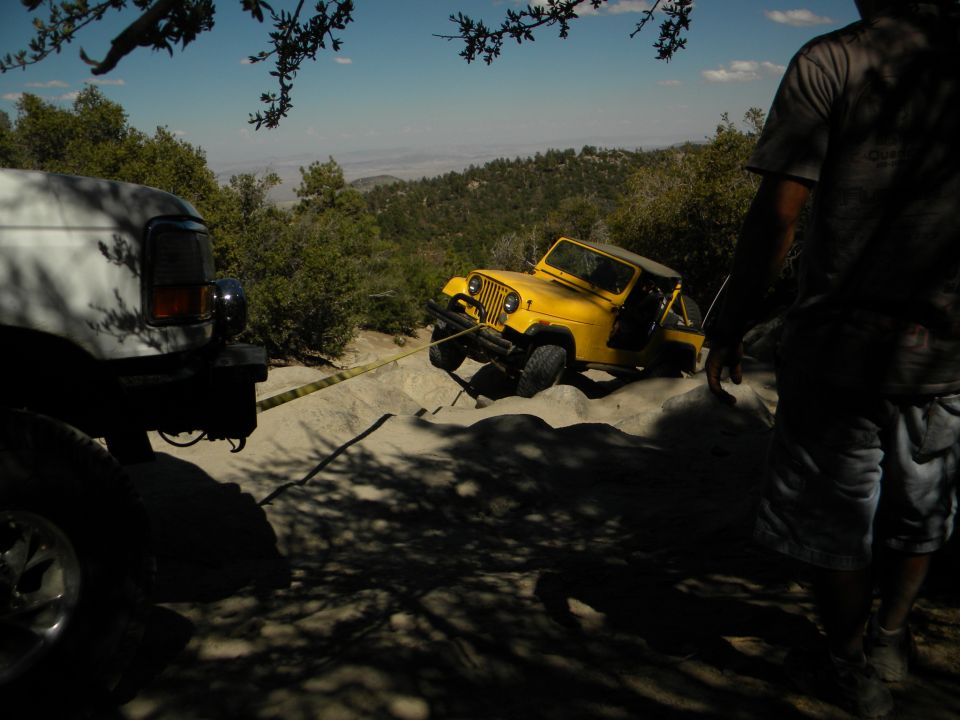 White truck pulling a yellow jeep out of a sandy ditch on a hill