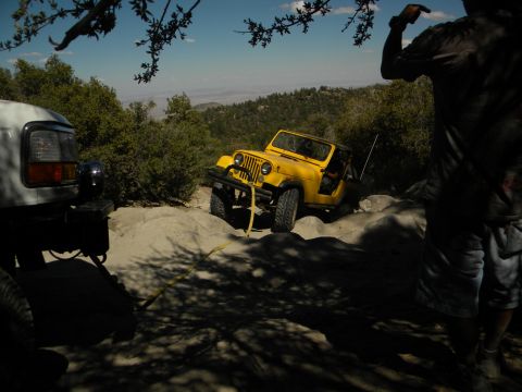 1992 Ford Bronco - A yellow Jeep Wrangler navigates a rocky trail, with a white SUV partially visible in the foreground.