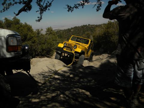1992 Ford Bronco - A yellow Jeep navigates a rocky off-road trail, with a white truck partially visible in the foreground.