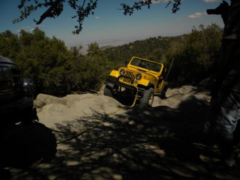 1992 Ford Bronco - A yellow Jeep navigates a challenging rocky terrain on a sunny day, with another vehicle assisting.