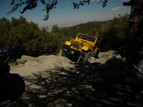 1992 Ford Bronco - A yellow Jeep Wrangler navigates a challenging rocky trail under a clear blue sky.