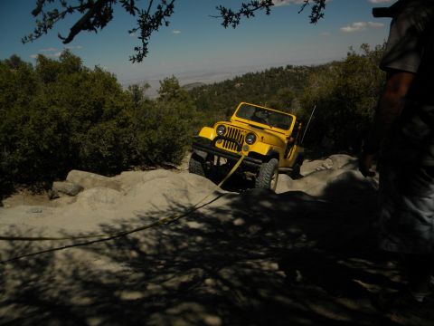 1992 Ford Bronco - A yellow Jeep Wrangler navigates a difficult rocky trail, using a tow strap for assistance.