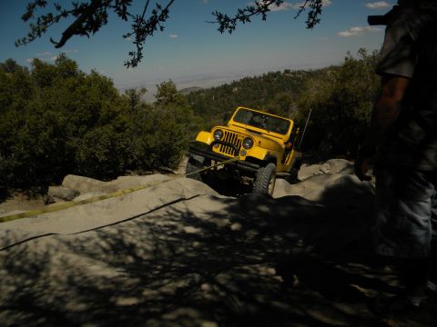 1992 Ford Bronco - A yellow Jeep CJ navigates a challenging rocky trail with assistance from a tow strap.