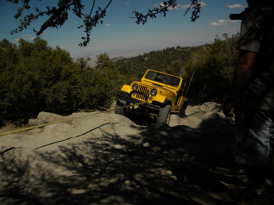 Yellow Jeep Wrangler on rocky terrain, being pulled by a yellow strap