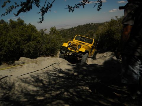 1992 Ford Bronco - A yellow Jeep Wrangler navigates a challenging rocky trail, being pulled by a tow strap.