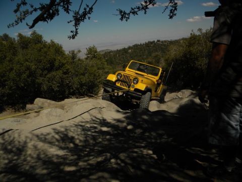 1992 Ford Bronco - Yellow Jeep Wrangler navigating a difficult rocky trail on a sunny day.