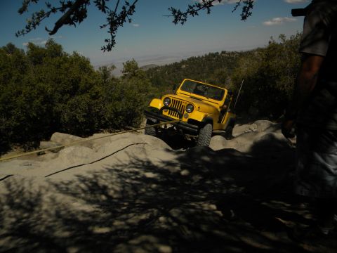 1992 Ford Bronco - A yellow Jeep Wrangler navigates a challenging rocky trail, assisted by a tow rope.
