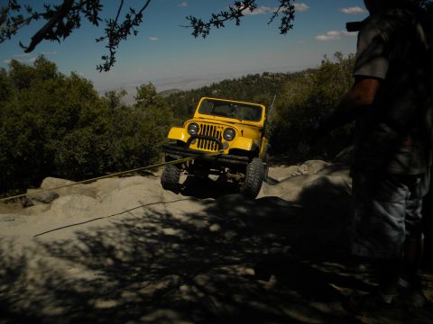 1992 Ford Bronco - A yellow Jeep navigates a challenging rocky path, assisted by a tow rope.