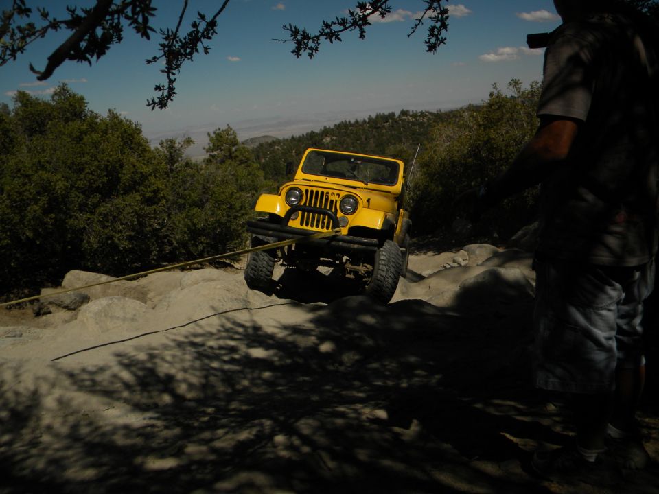 Yellow Jeep being pulled by a rope on a rocky trail