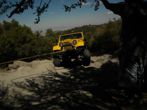 1992 Ford Bronco - Yellow Jeep CJ navigating a steep, rocky trail on a sunny day.